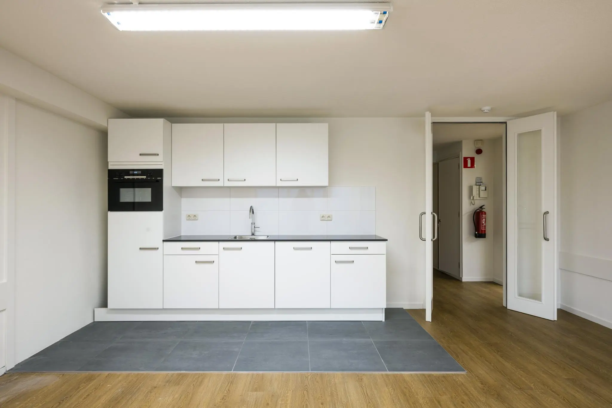 Moderne witte keuken met ingebouwde oven en grijze tegels in een appartement aan de Prins Hendrikkade.